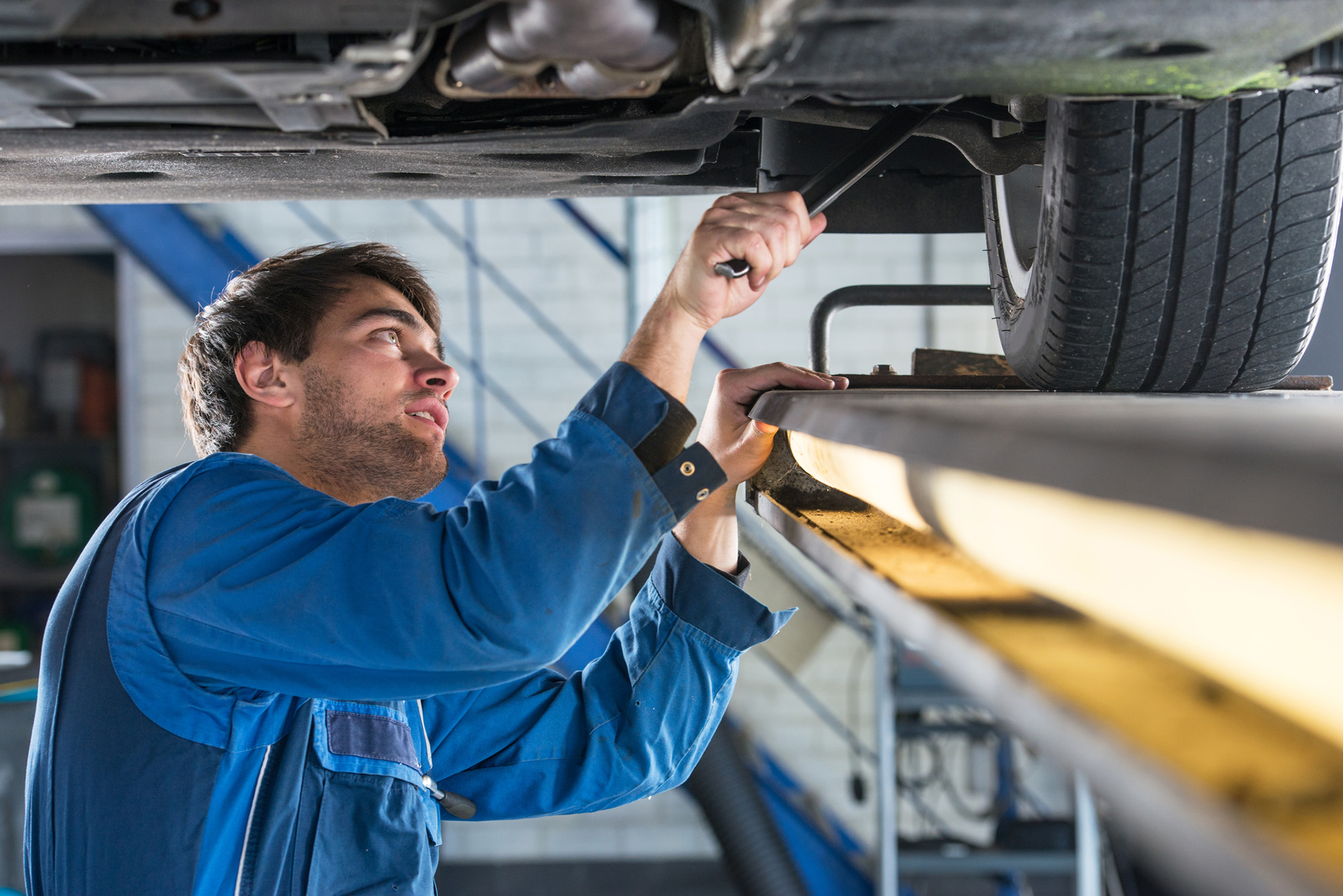 Mechanic, examining the suspension of a vehicle with a steel rod for any undesired clearances as part of a periodical vehicle safety inspection or mot test