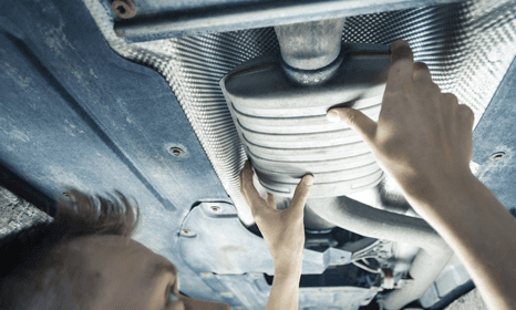 Man fixing a car exhaust while car is on ramp
